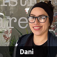 A smiling person with glasses, a black headband, and a nose ring stands in front of a glass window with white lettering. The name "Dani" is displayed in bold white text at the bottom of the image.